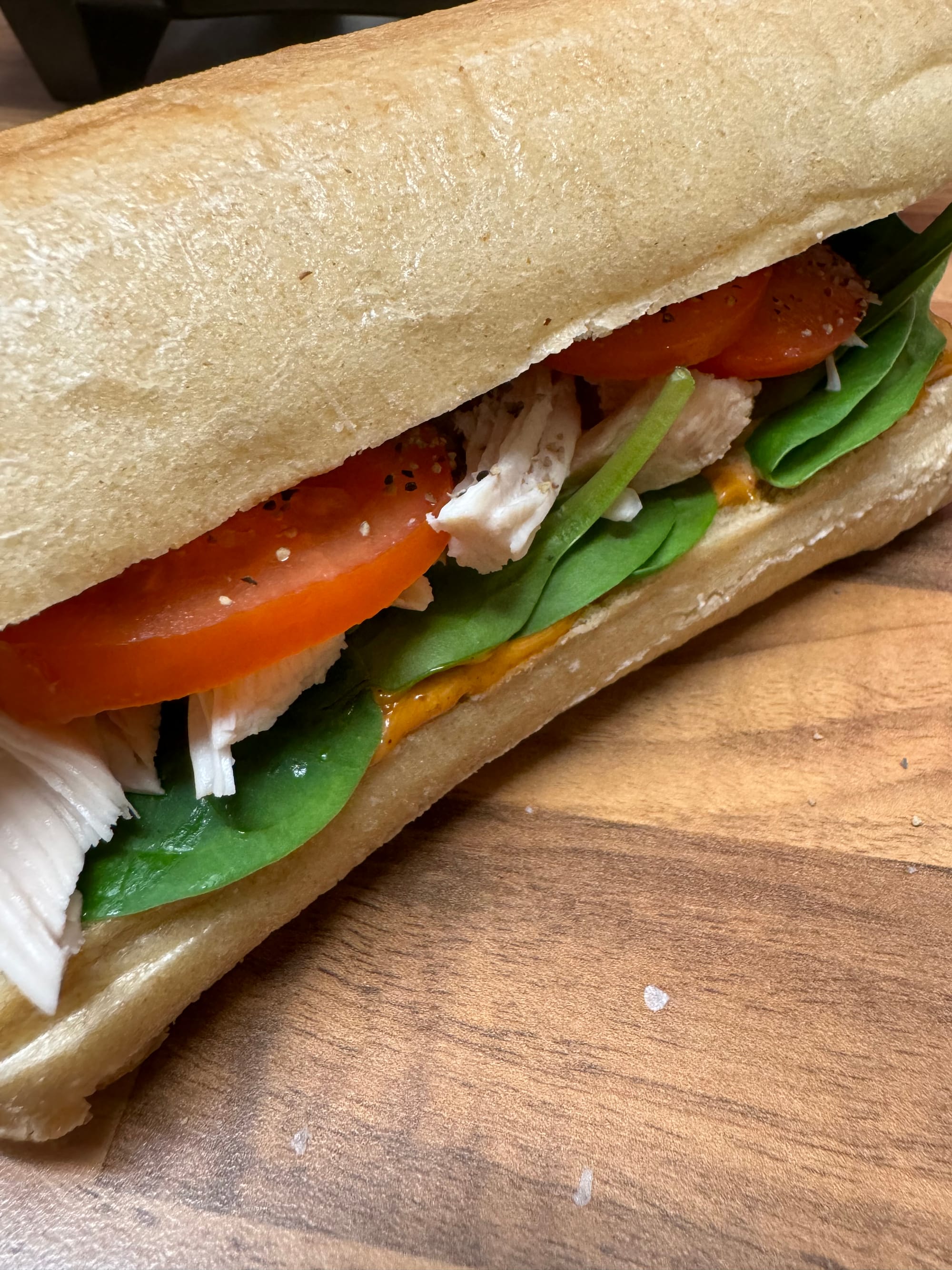 A delicious sandwich with juicy tomatoes and tender chicken, placed on a rustic wooden table.