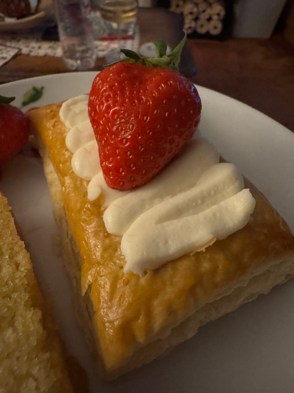 Golden puff pastry Danish filled with strawberry jam and topped with piped cream cheese filling and a fresh strawberry on a white plate