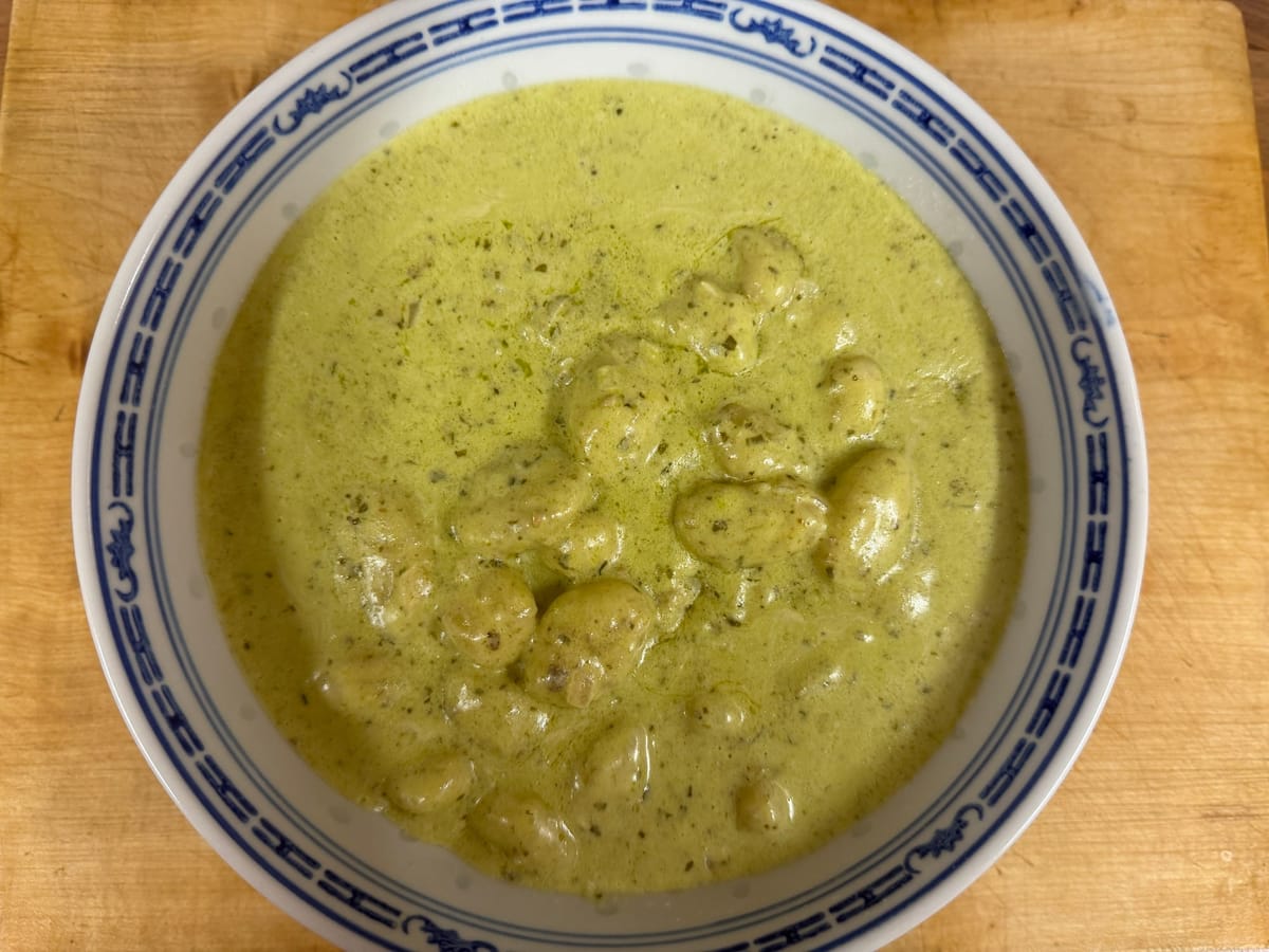 Bowl of creamy garlic pesto gnocchi with golden pillowy dumplings in green pesto cream sauce