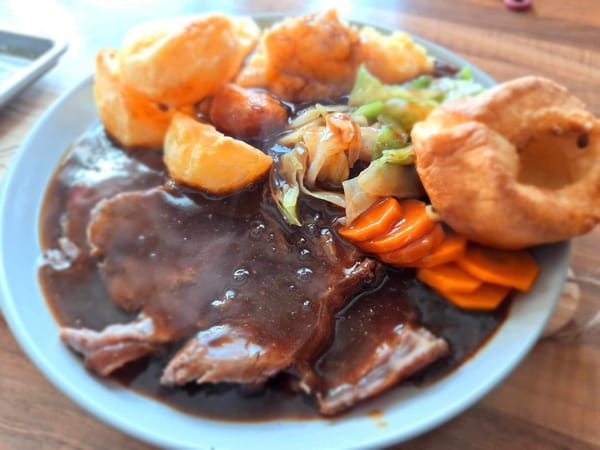 Traditional Sunday Roast Beef dinner with Yorkshire puddings, crispy roast potatoes, carrots, cabbage and gravy on vintage plate