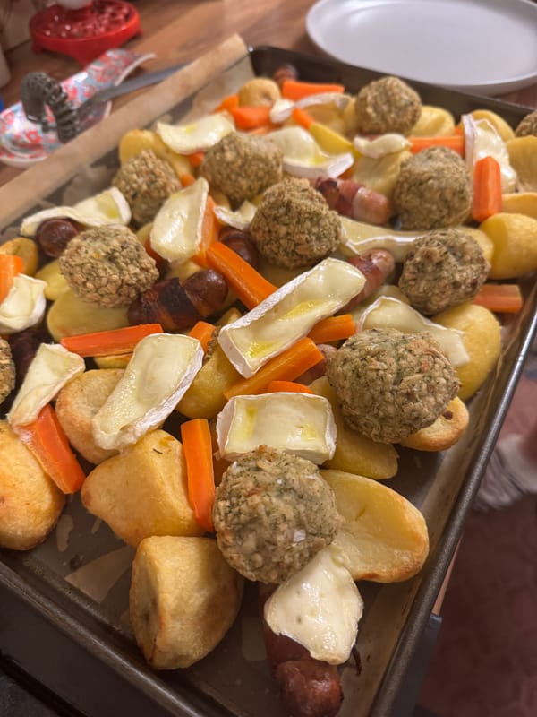 Baked potatoes, carrots, stuffing, and brie on a baking sheet.