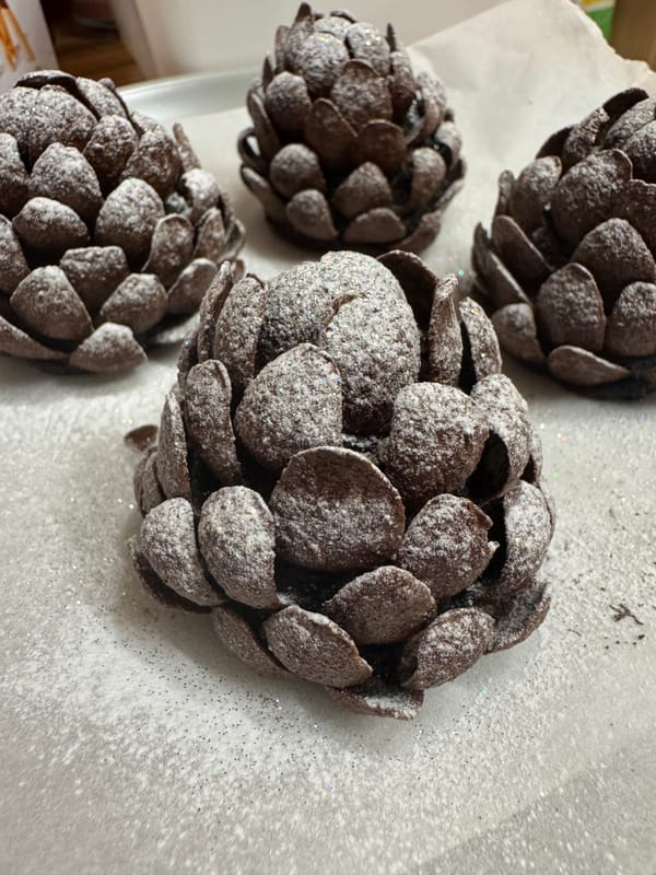 A group of four chocolate pinecones dusted with powdered sugar on a baking sheet.