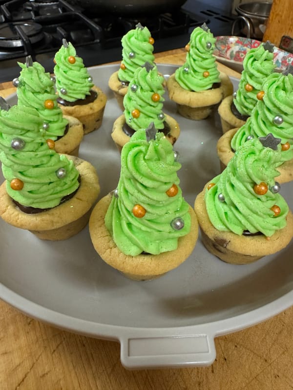 Chocolate chip cookie cups filled with green frosting, topped with sprinkles and chocolate stars, resembling Christmas trees.