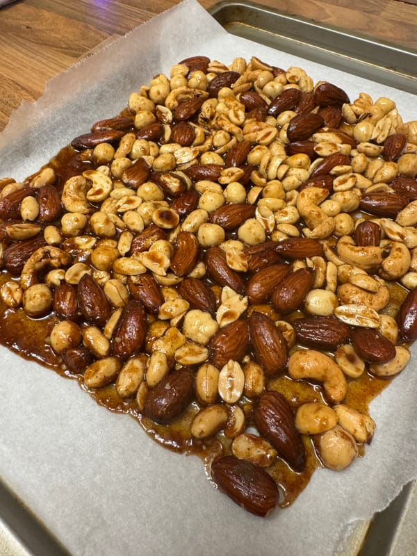 A tray of roasted mixed nuts, including almonds, cashews, and peanuts, coated in a caramelized glaze.