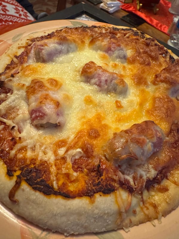 A close-up of a pizza with a golden crust, tomato sauce, melted mozzarella cheese, and cooked sausage.