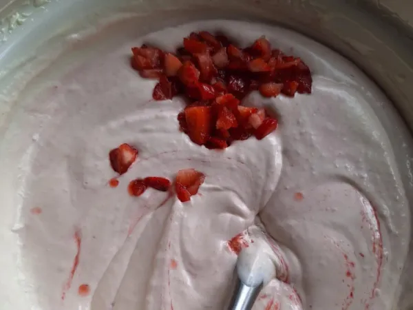 Chunky strawberry ice cream mixture with diced fresh strawberries folded into creamy pink base before freezing