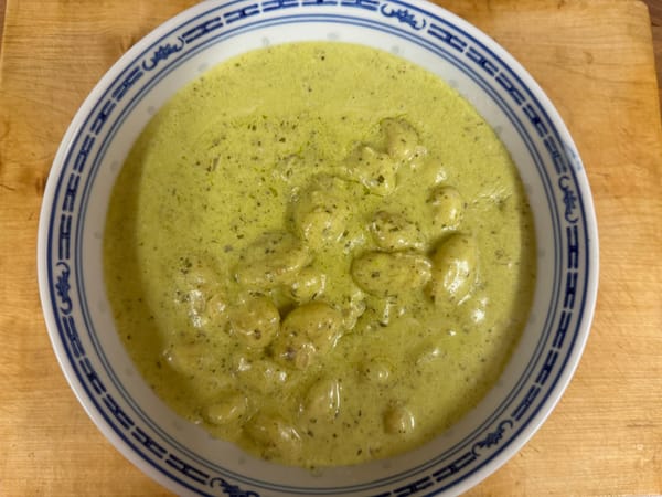 Bowl of creamy garlic pesto gnocchi with golden pillowy dumplings in green pesto cream sauce
