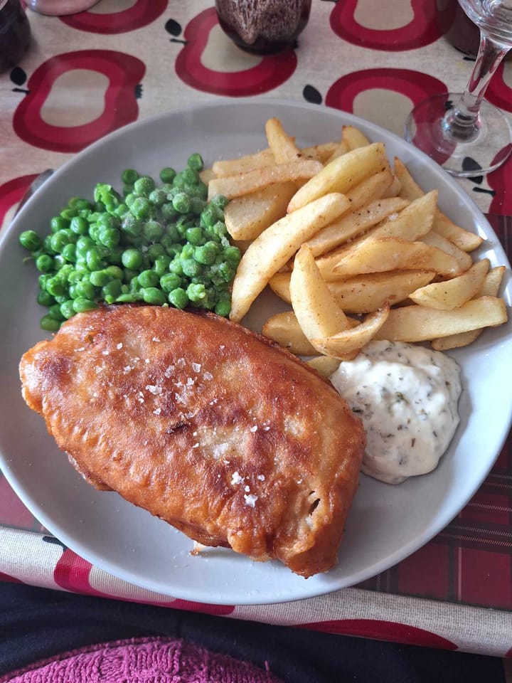 Golden brown, crispy beer-battered fish & chips with fluffy white fish inside. Served on a plate with green peas.